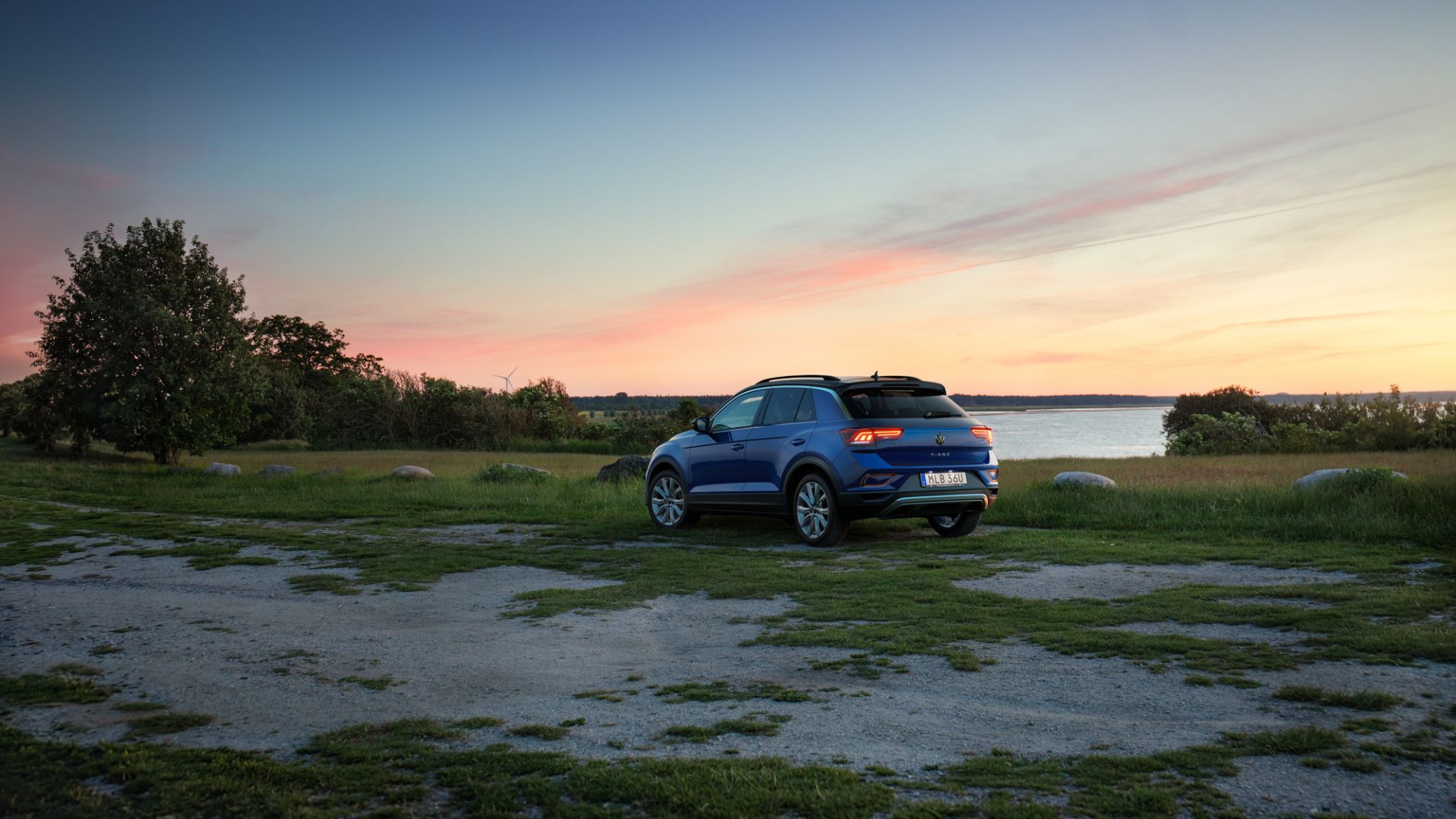blå t-rov parkerad på en grusplan med hav och himmel med solnedgång bakom