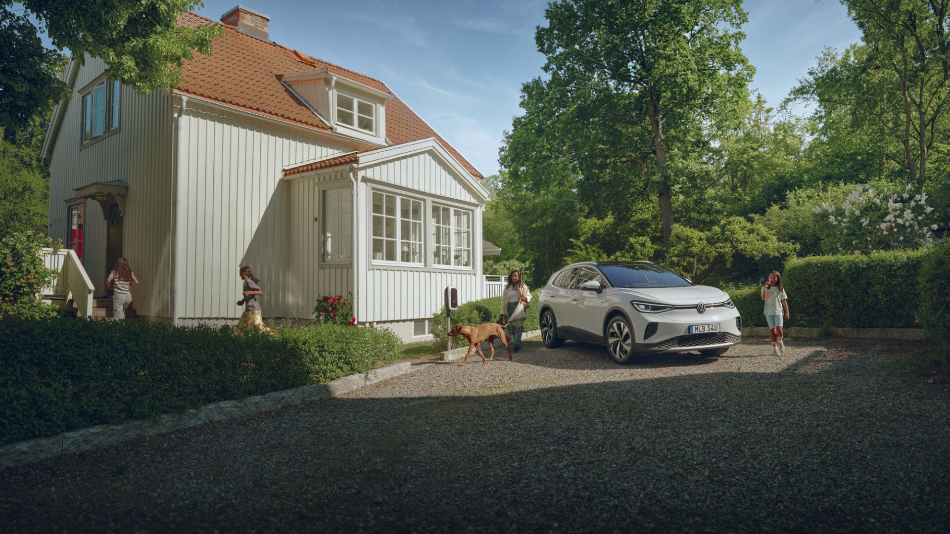 ID.4 po parkerad på en grusplan framför en villa med en familj oh en hund som packar in sig i bilen.