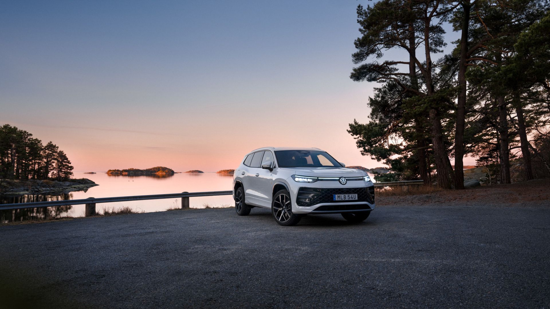 vit tayron parkerad på en grusplan med hav och himmel med solnedgång bakom